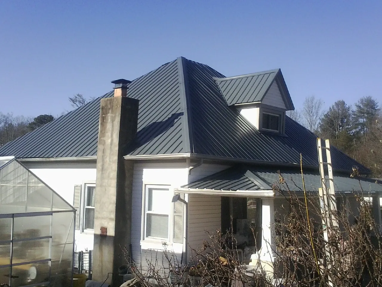Dark blue standing seam metal roof on a white farmhouse with dormer — Slate & Tile Roof Repair by Roofing Brothers in Moncks Corner