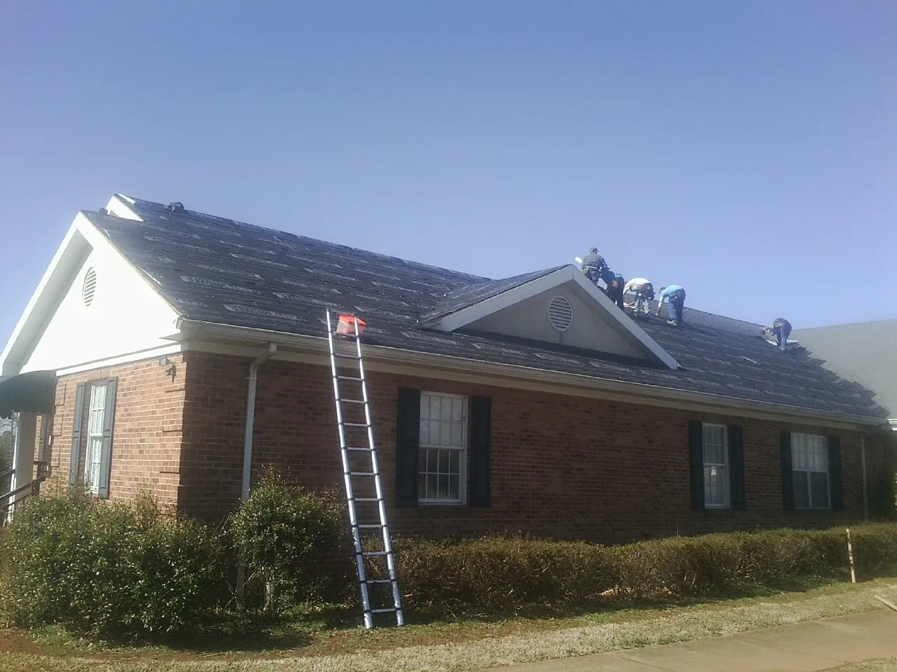Crew tearing shingles off a brick ranch roof with a ladder set — Metal Roof Repair work by our crew in Moncks Corner